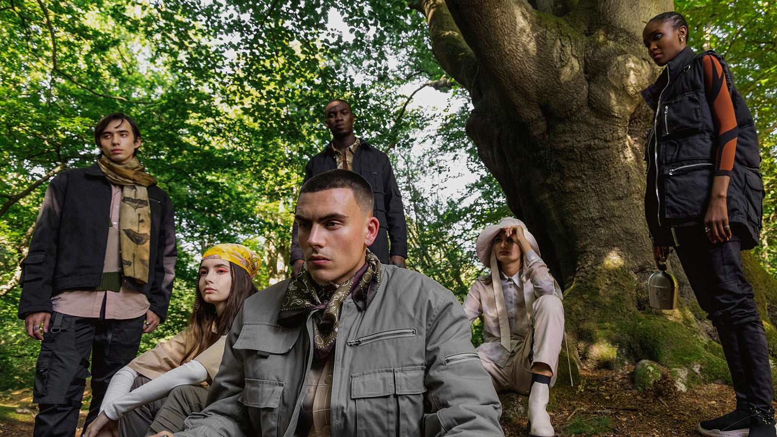 Six models wearing cargo pants and jackets pose in  a forest.