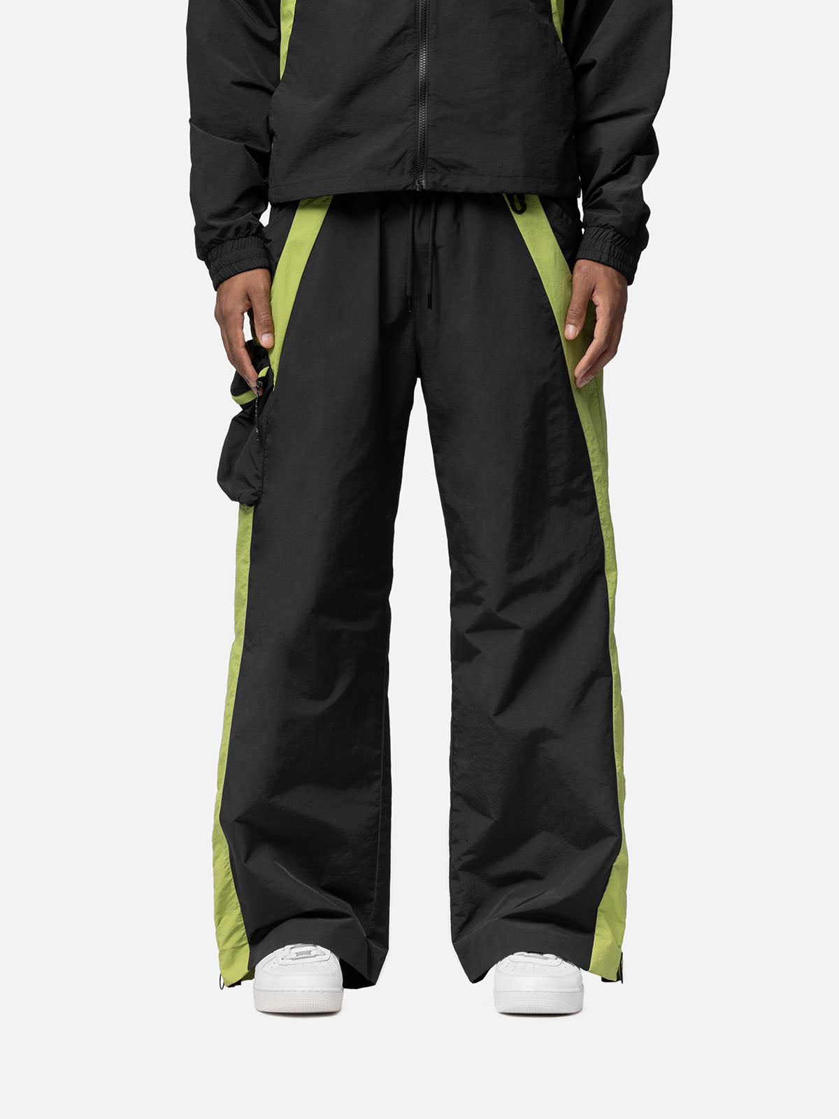 Black with green side panels track pants, with side pocket on the right side, decorative buckle at the waist, matching jacket, and white sneakers.