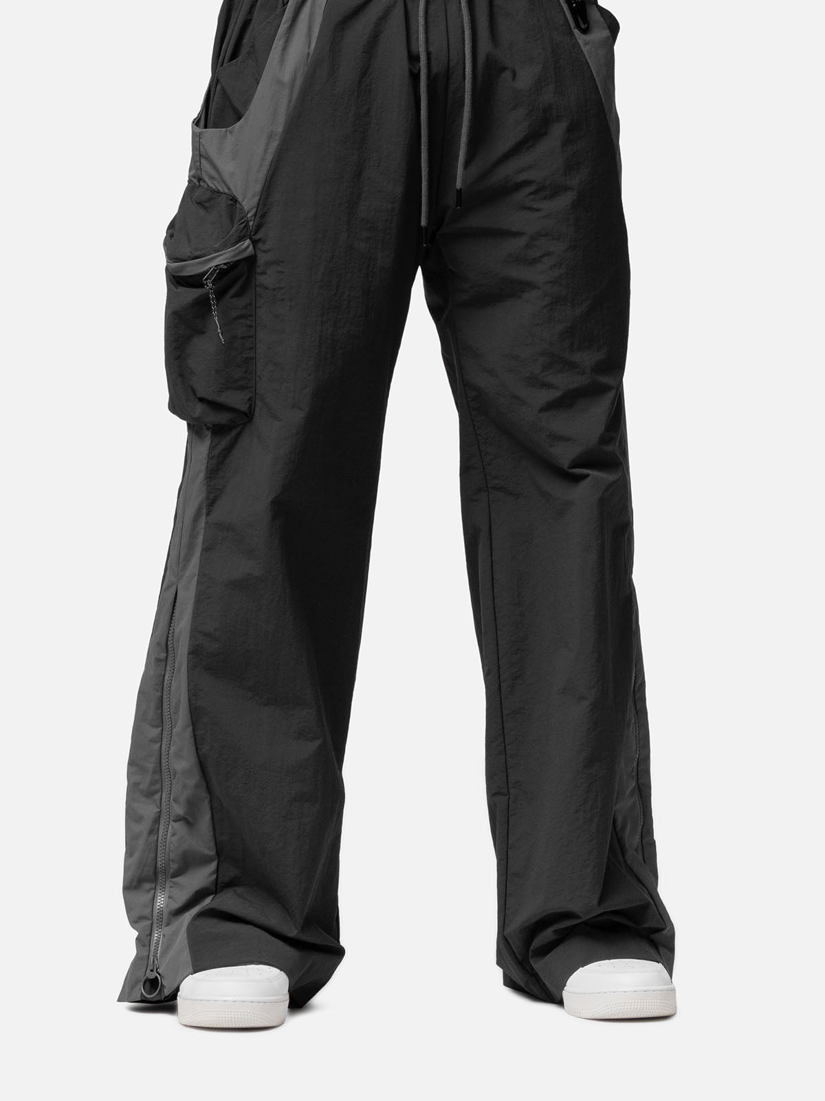 Close-up of the side pocket and a zip-up expandable seam to hem of a charcoal with grey side panels track pants.