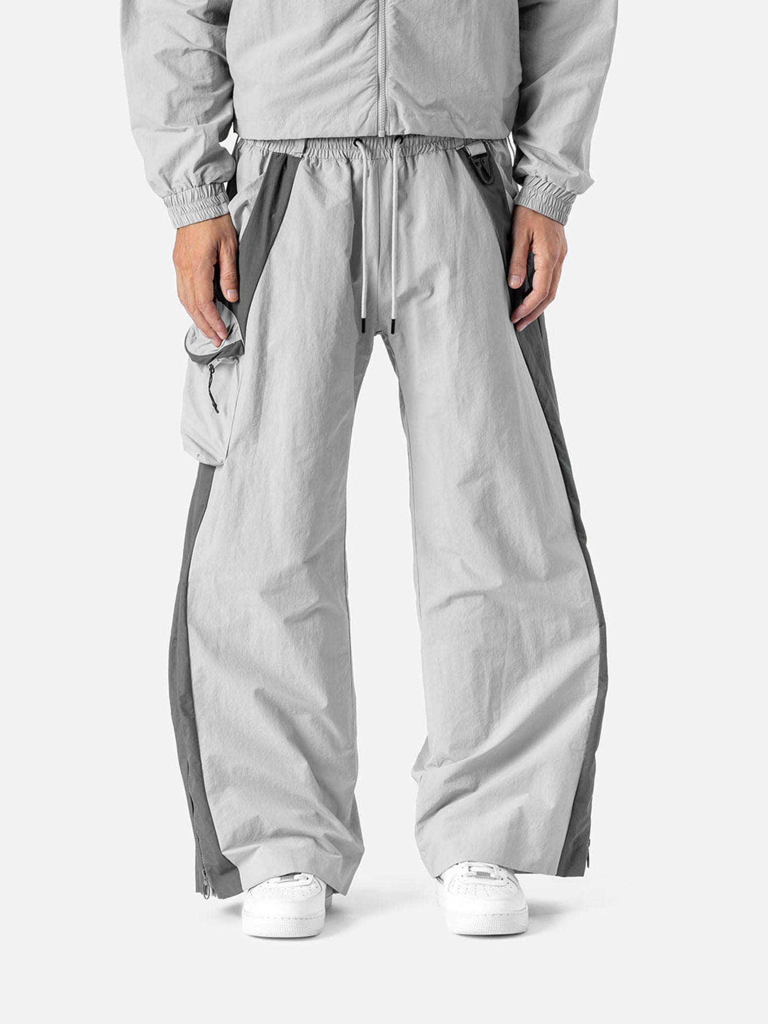 Light grey with grey side panels track pants, with side pocket on the right side, decorative buckle at the waist, matching jacket, and white sneakers.