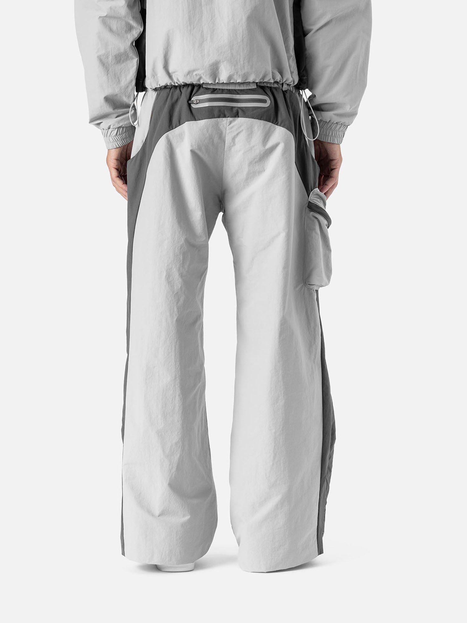 Back view of a light grey with grey side panels track pants, side pocket on the right side, zip pocket at the back, matching jacket, and white sneakers.