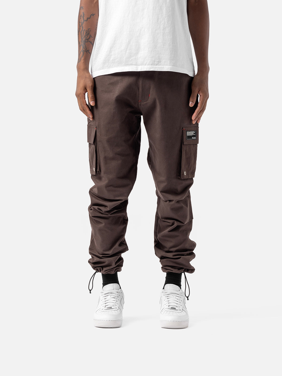Bark cargo pants with side pockets, ankle drawstrings, paired with a white t-shirt, and white sneakers, showcasing streetwear style.