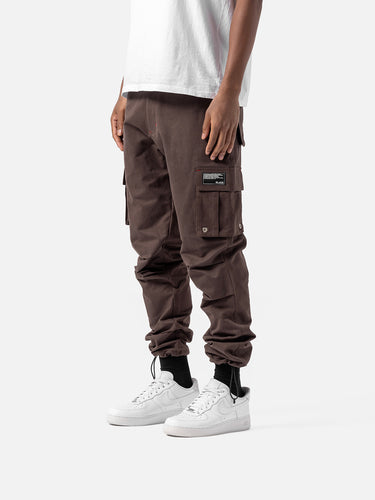 Side view of bark cargo pants with side pockets, ankle drawstrings, paired with a white t-shirt, and white sneakers.