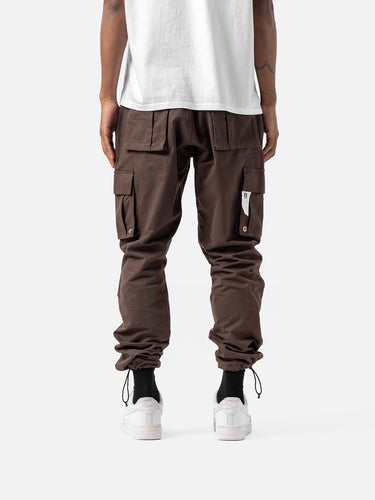 Back view of bark cargo pants with side pockets, ankle drawstrings, and simple back pockets, paired with a white t-shirt, and white sneakers.