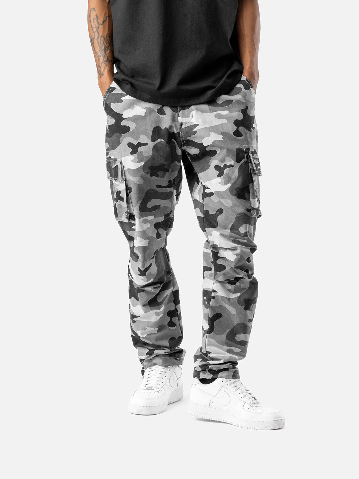 Front view of grey camo cargo pants with side pockets, ankle drawstrings, paired with a black t-shirt, and white sneakers.