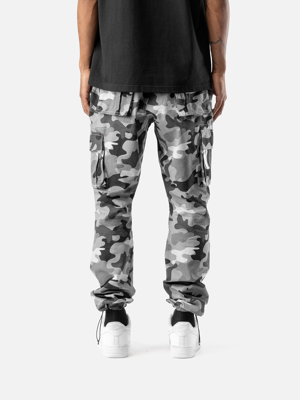 Back view of grey camo cargo pants with side pockets, ankle drawstrings, and simple back pockets, paired with a black t-shirt, and white sneakers.