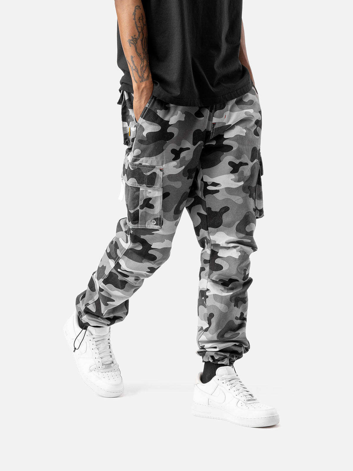 Side view of grey camo cargo pants with side pockets, ankle drawstrings, paired with a black t-shirt, and white sneakers.