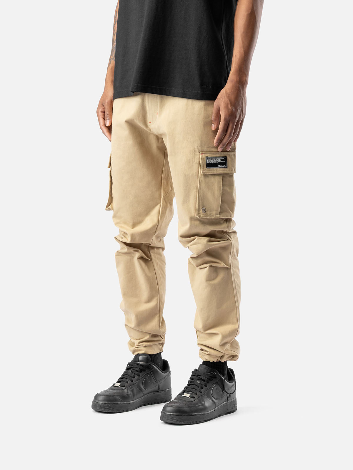 Side view of khaki cargo pants with side pockets, ankle drawstrings, paired with a black t-shirt, and black sneakers.