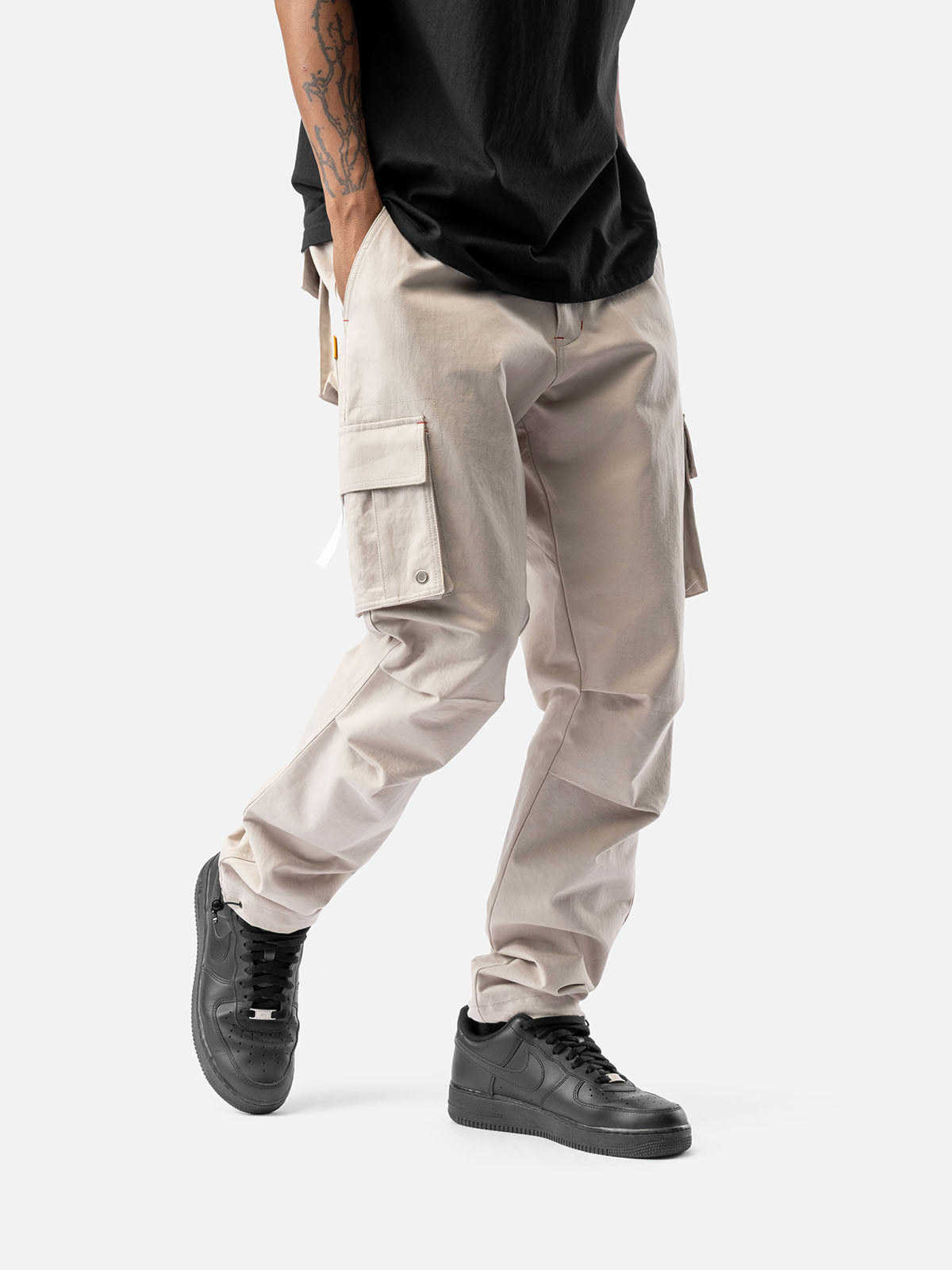 Side view of rock cargo pants with side pockets, ankle drawstrings, paired with a black t-shirt, and black sneakers.
