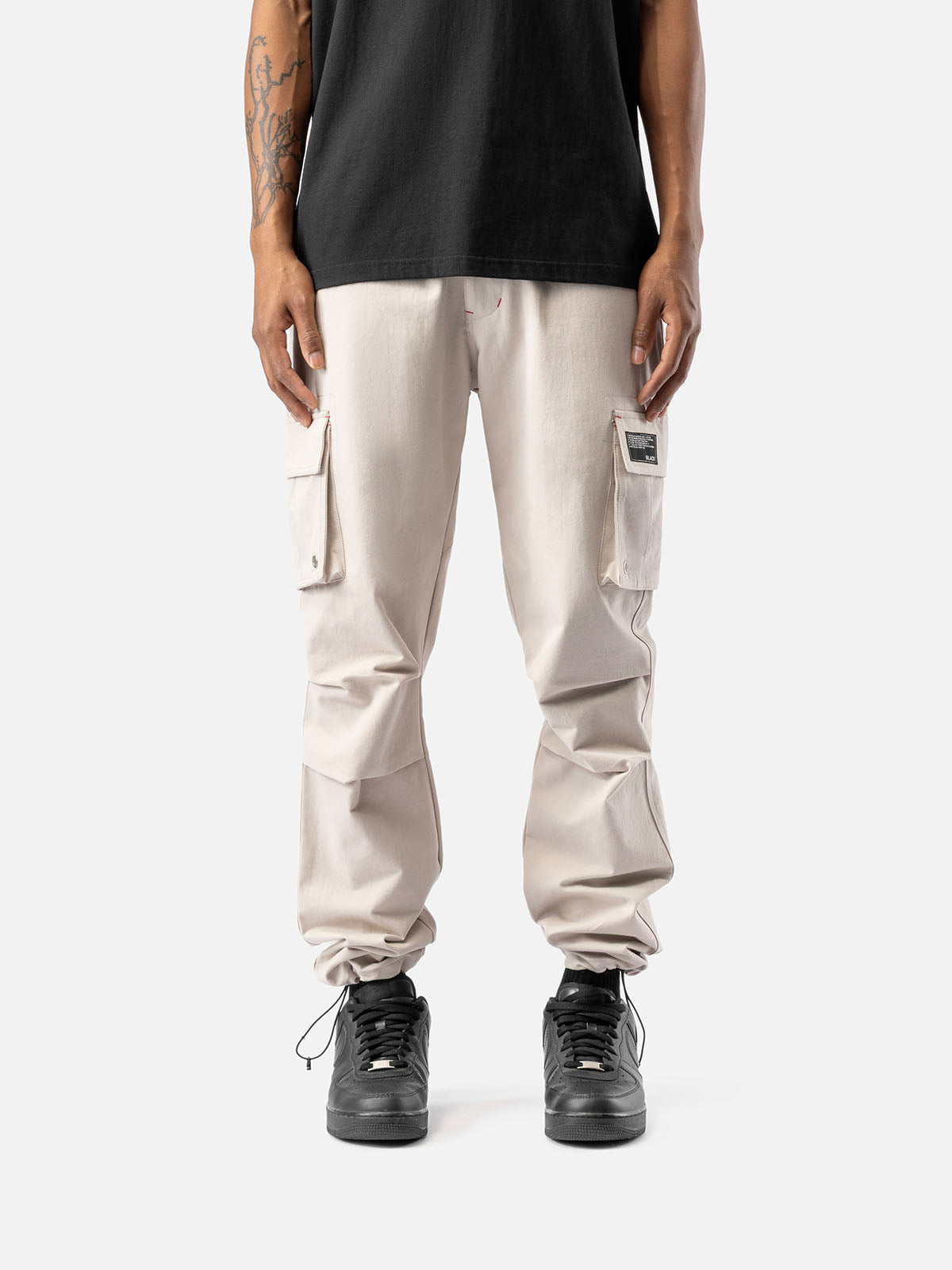 Rock cargo pants with side pockets, ankle drawstrings, paired with a black t-shirt, and black sneakers, showcasing streetwear style.