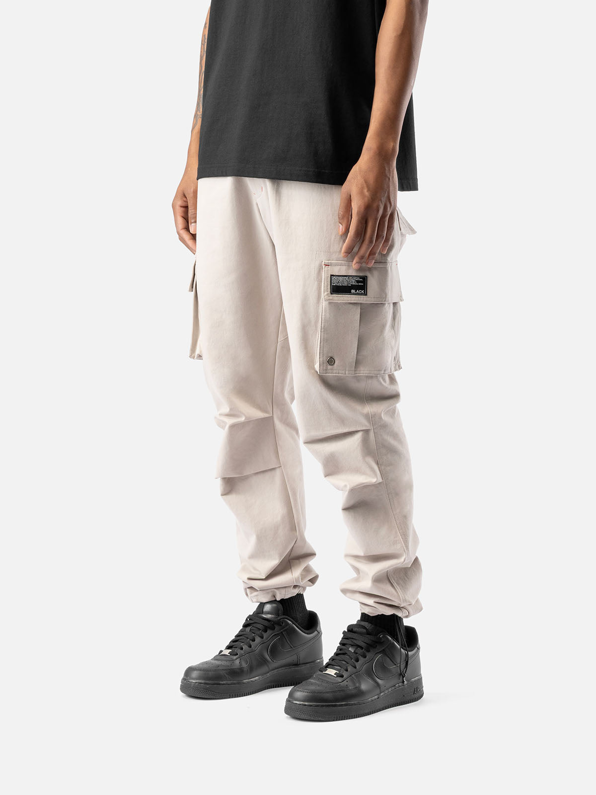Side view of rock cargo pants with side pockets, ankle drawstrings, paired with a black t-shirt, and black sneakers.