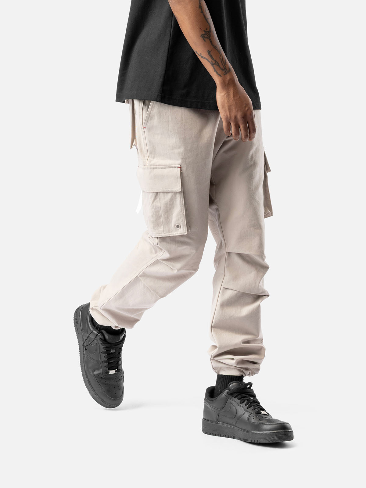 Side view of rock cargo pants with side pockets, ankle drawstrings, paired with a black t-shirt, and black sneakers.
