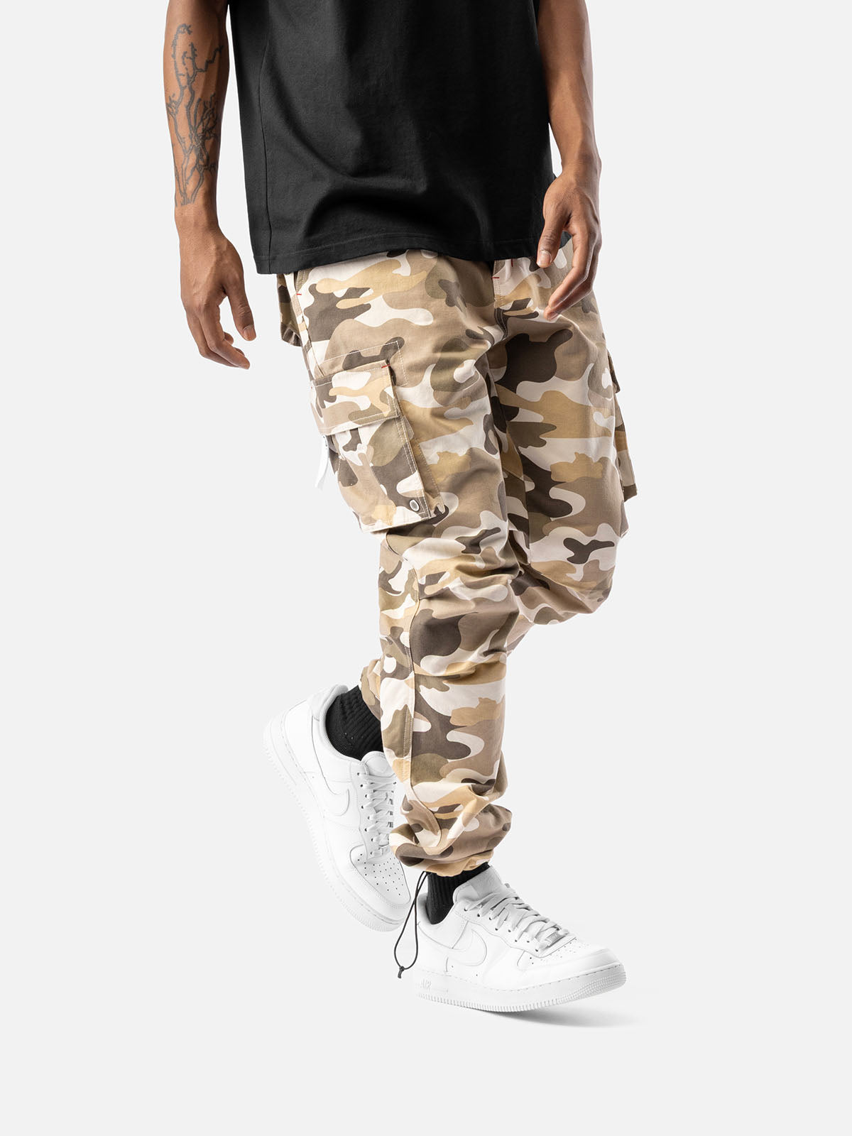 Side view of sand camo cargo pants with side pockets, ankle drawstrings, paired with a black t-shirt, and white sneakers.