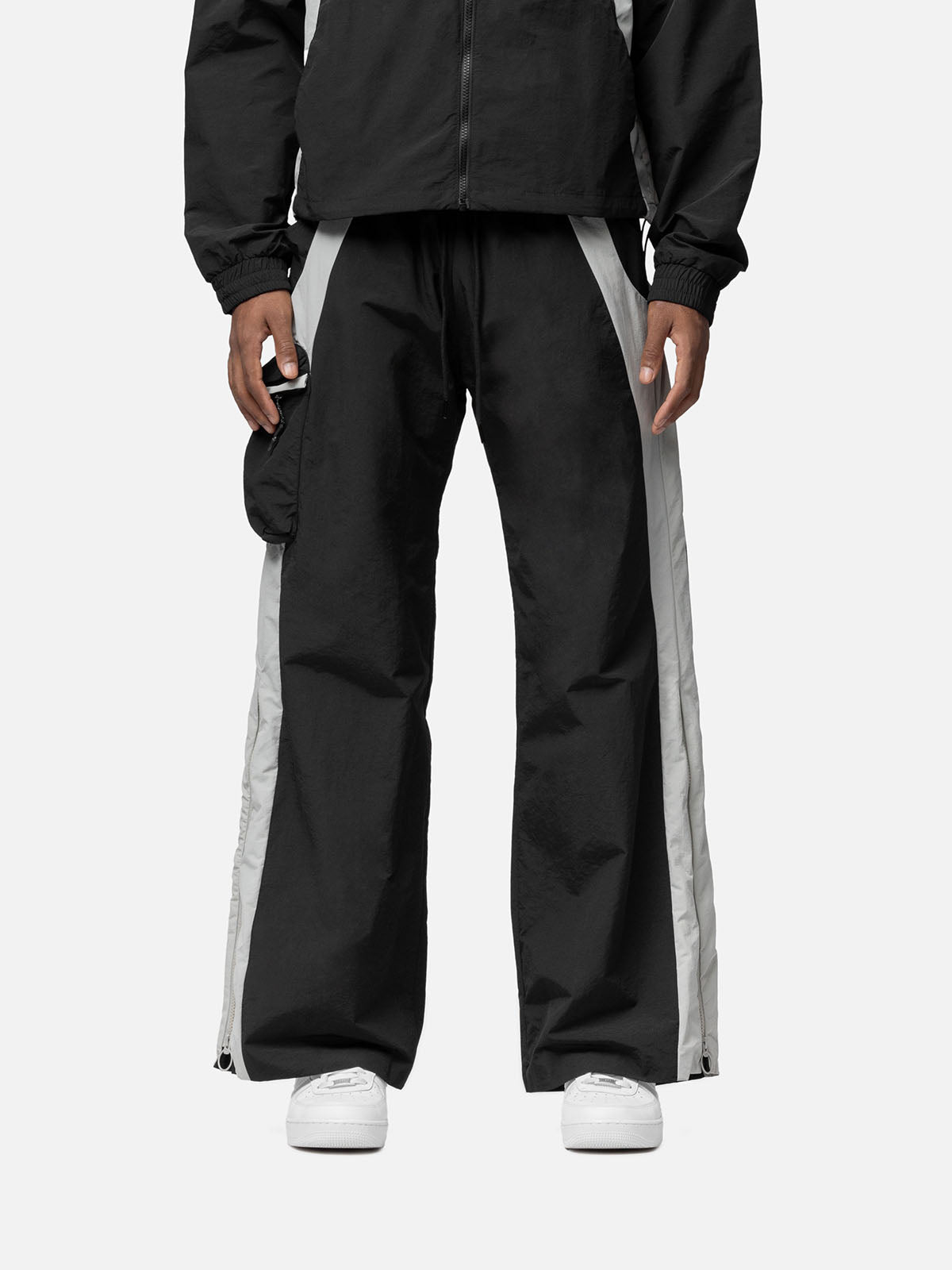 Black with white side panels track pants, with side pocket on the right side, decorative buckle at the waist, matching jacket, and white sneakers.