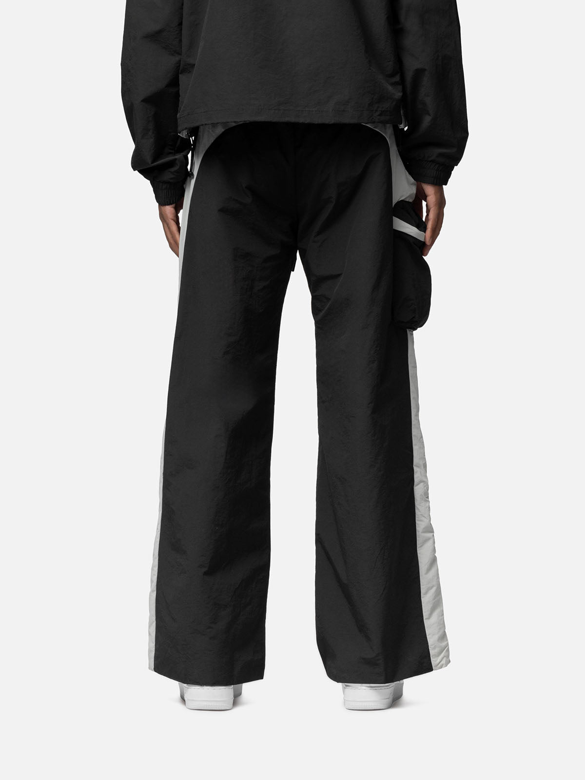 Back view of black with white side panels track pants, side pocket on the right side, zip pocket at the back, matching jacket, and white sneakers.