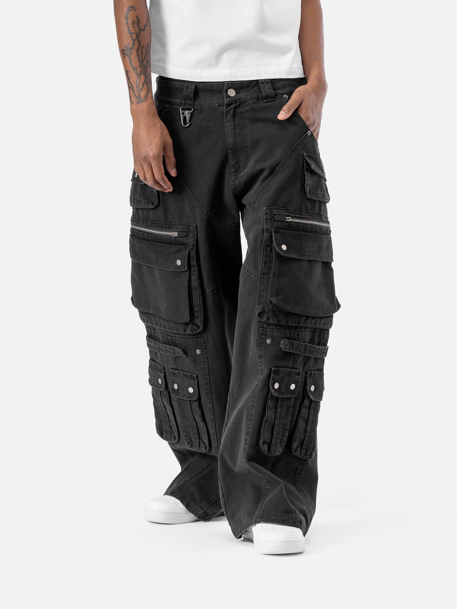 Front view of black cargo pants with multiple functional pockets, including flap and zipper pockets, paired with white sneakers and a white t-shirt.