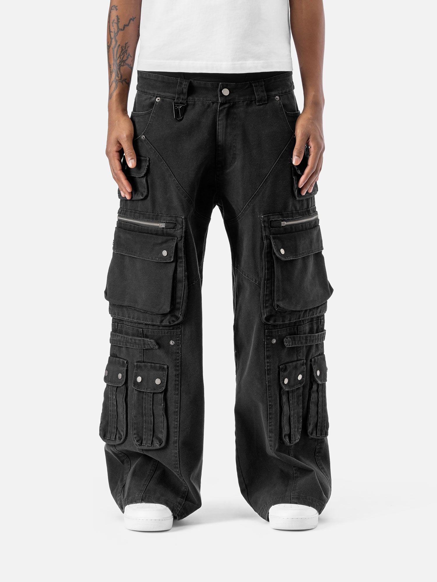 Black cargo pants with multiple large pockets and zipper details, paired with a white t-shirt and sneakers, showcasing streetwear style.