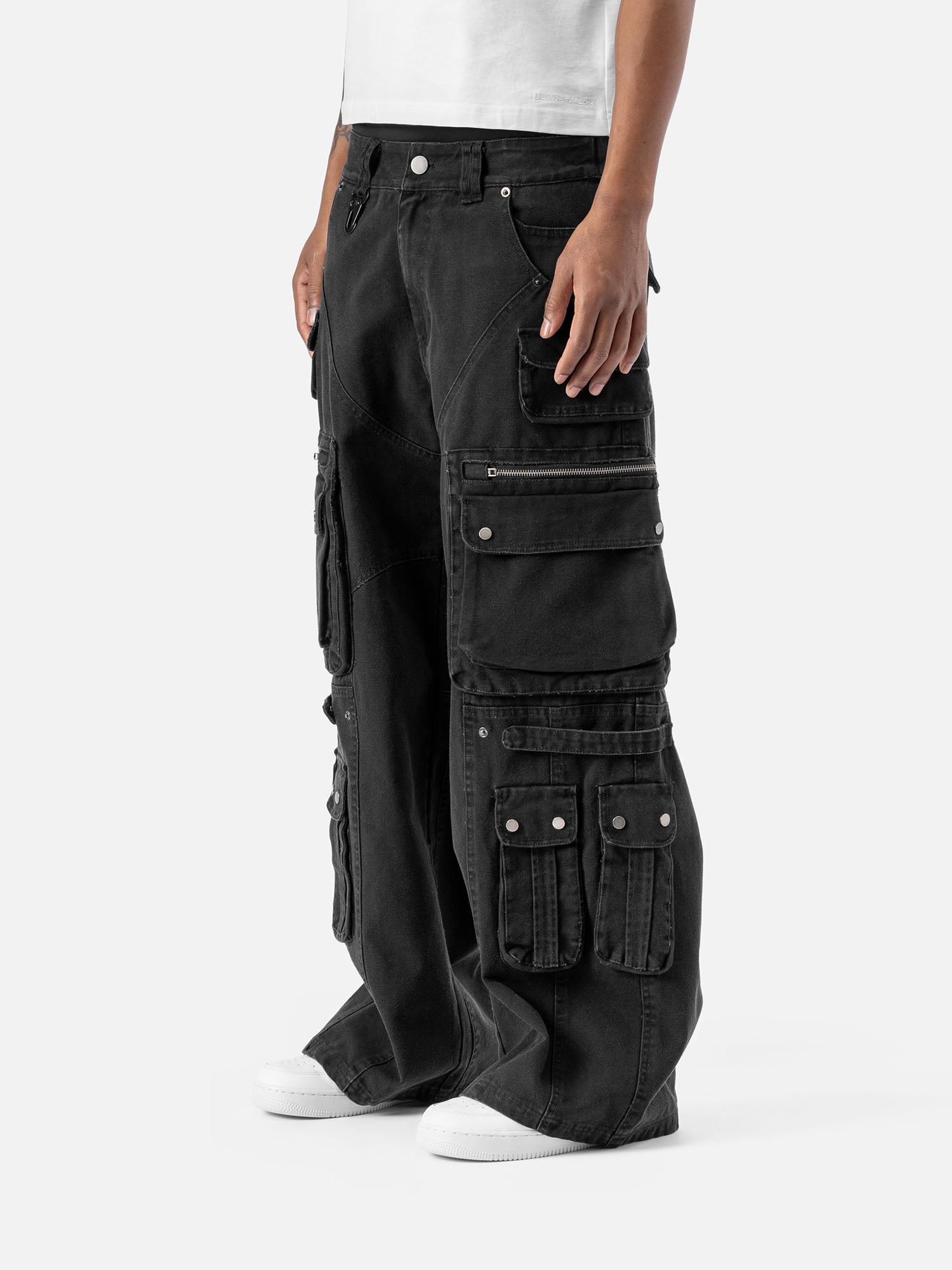 Side view of black cargo pants with multiple large pockets, a wide-leg cut, and paired with a white t-shirt and sneakers.