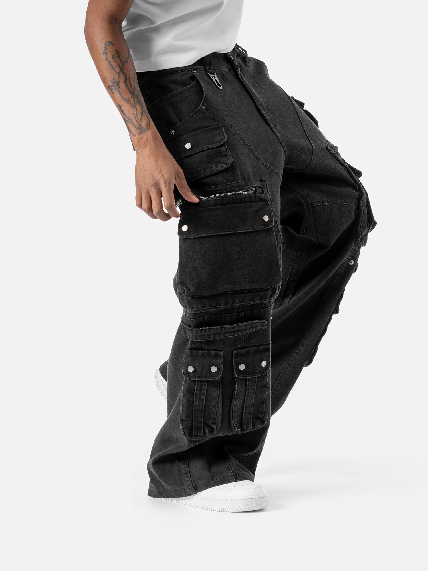Side view of black cargo pants with multiple functional pockets, including flap and zipper pockets, paired with white sneakers and a white t-shirt.