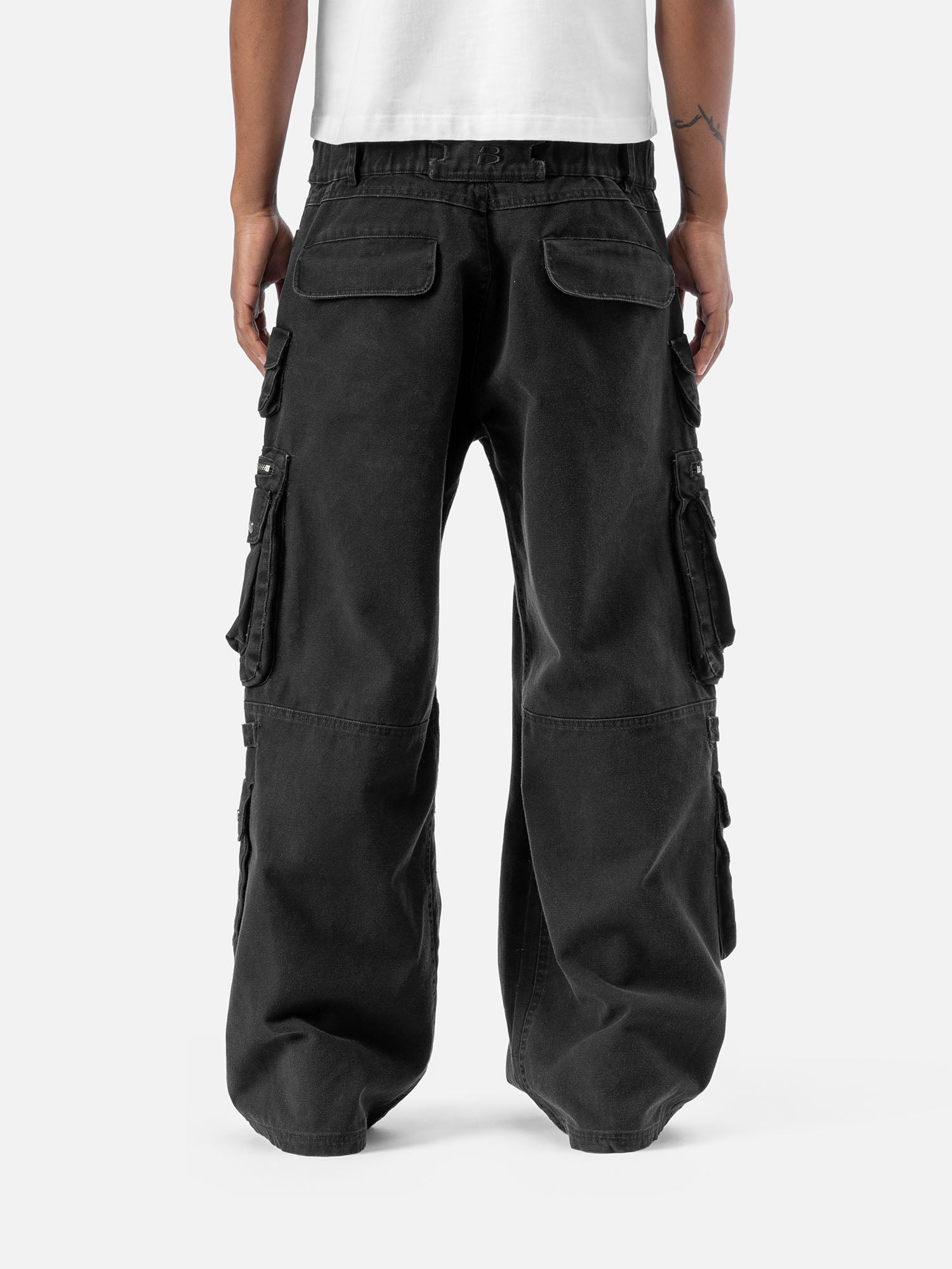 Back view of black cargo pants with large side pockets, a wide-leg cut, and simple back pockets, styled with a white t-shirt.