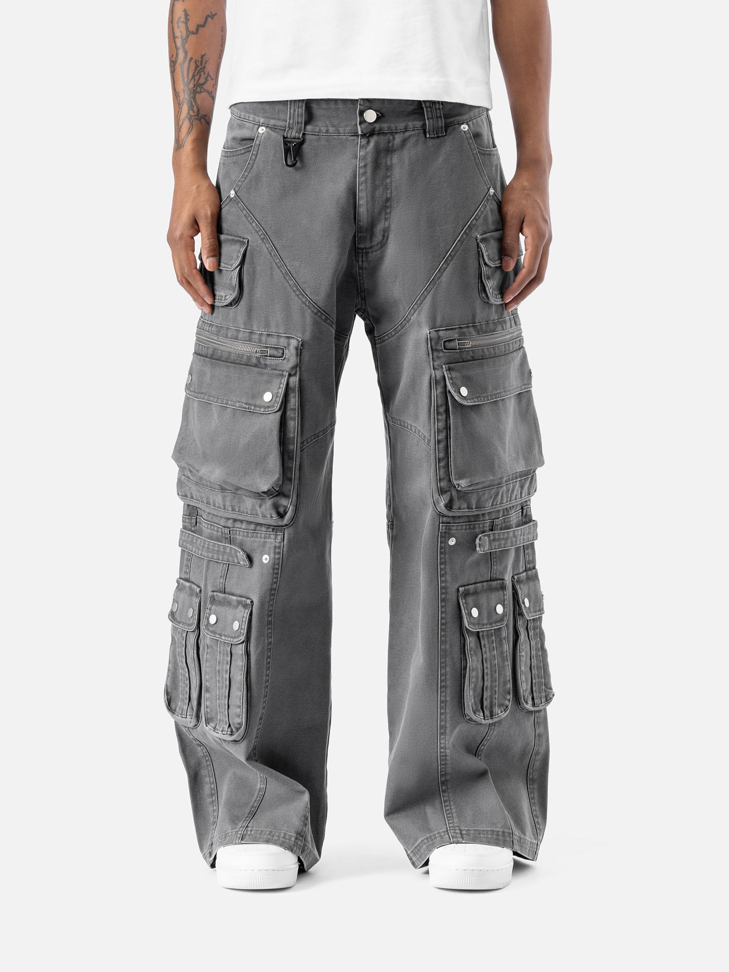 Grey cargo pants with multiple large pockets and zipper details, paired with a white t-shirt and sneakers, showcasing streetwear style.