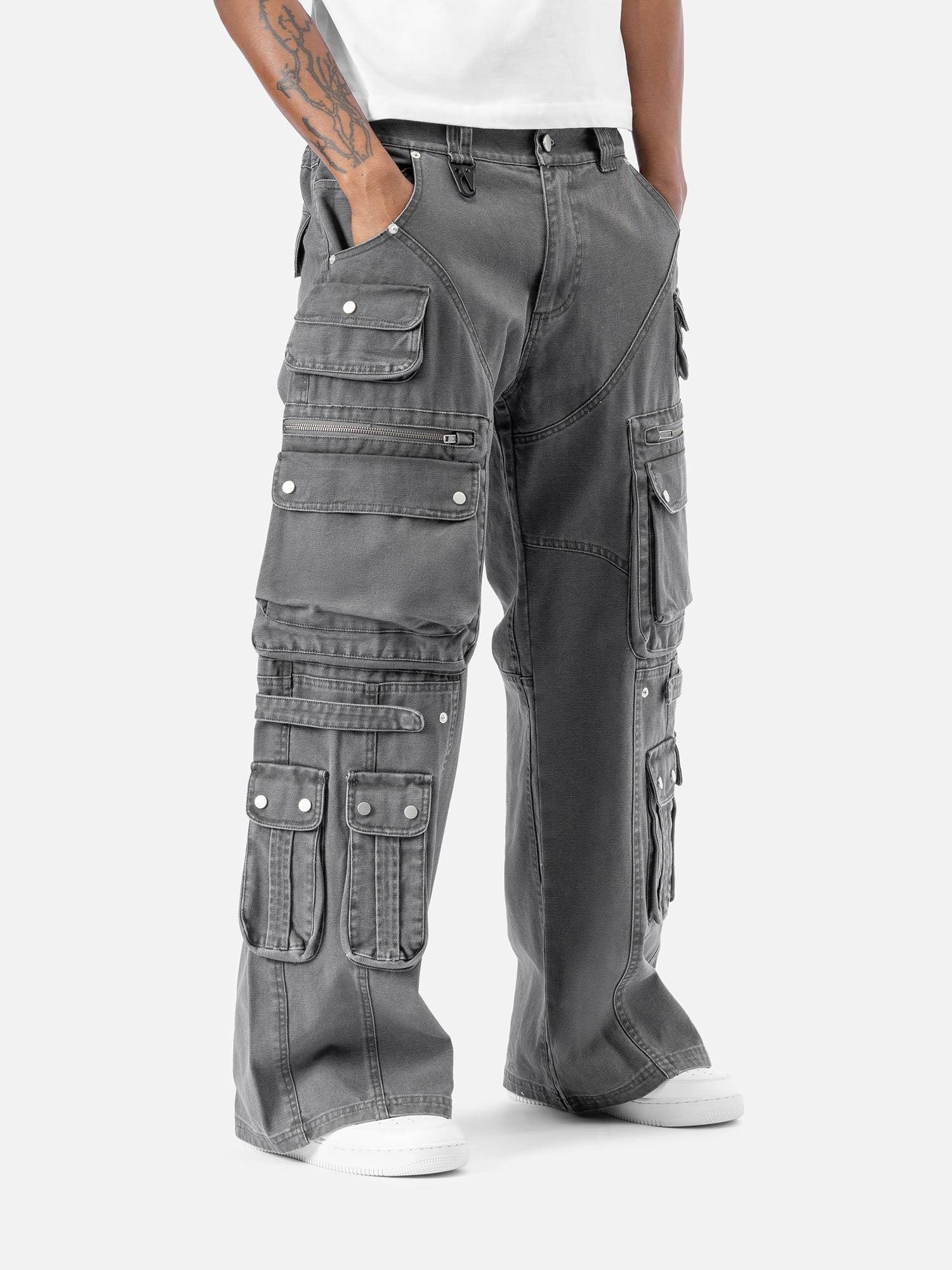 Side view of grey cargo pants with multiple functional pockets, including flap and zipper pockets, paired with white sneakers and a white t-shirt.