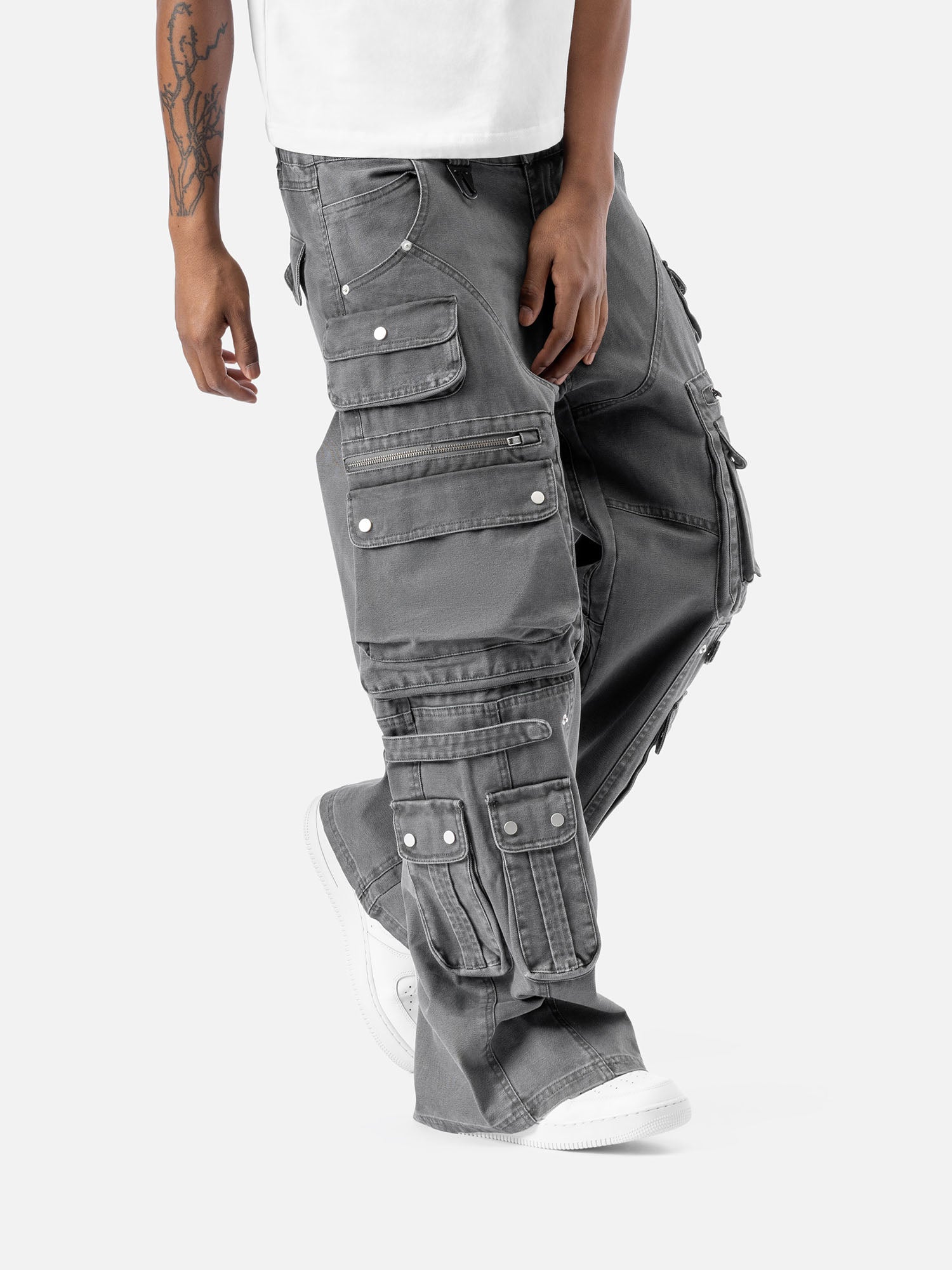 Side view of grey cargo pants with multiple functional pockets, including flap and zipper pockets, paired with white sneakers and a white t-shirt.
